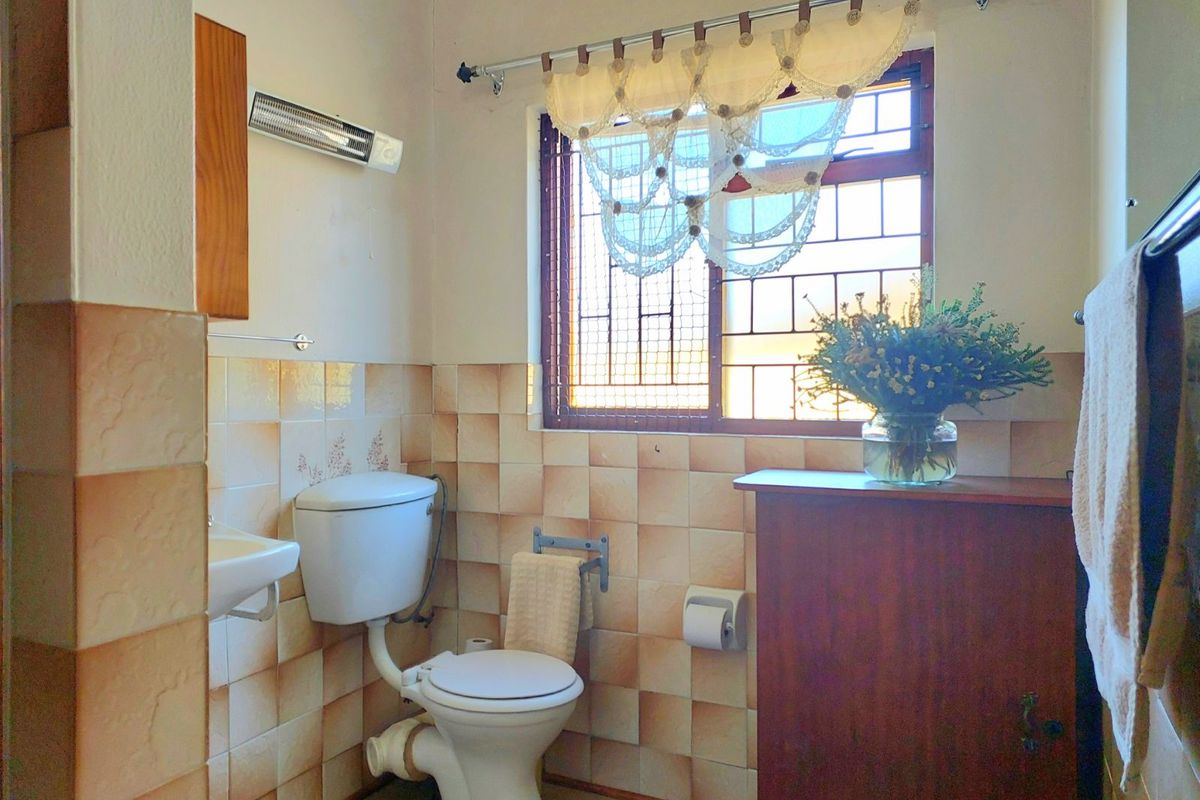 A functional bathroom featuring a wall-mounted basin, toilet, and window with security bars, finished with dated ceramic wall tiles.
