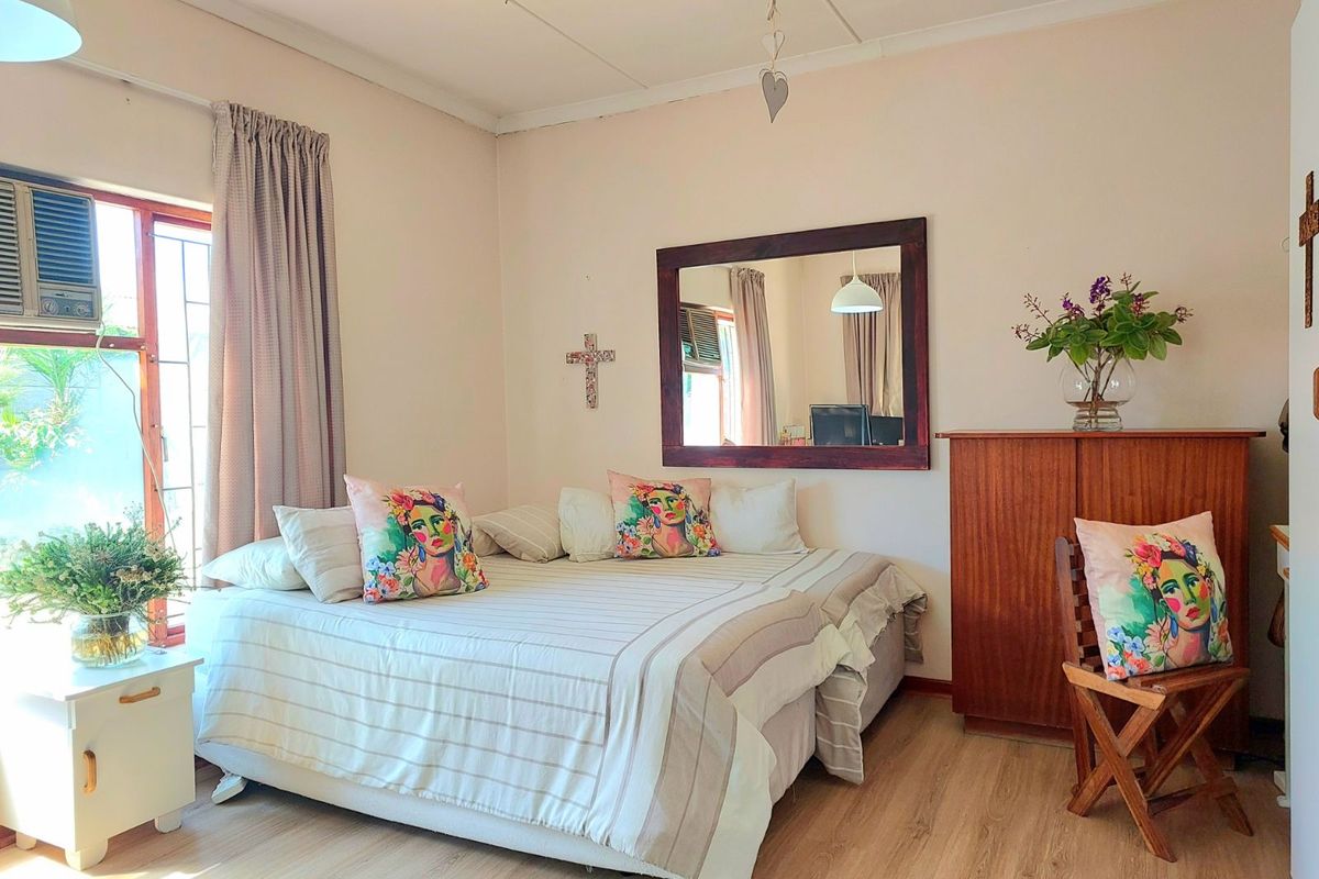 A well-lit bedroom featuring light wood-look flooring, a built-in window air conditioning unit, and neutral wall finishes.