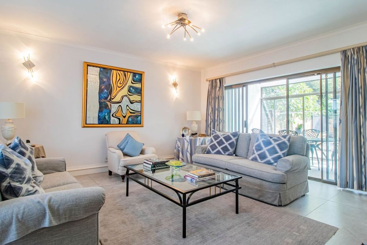 A bright and spacious living room featuring tiled flooring, modern wall sconces, and large sliding glass doors that provide access to the outdoor patio area.