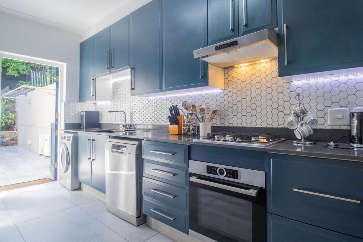 Modern kitchen featuring dark blue cabinetry, stone countertops, a hexagonal tile backsplash, integrated oven, gas hob, and an extractor fan.