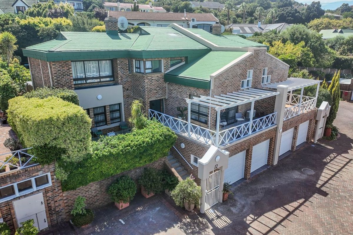 Aerial view of a multi-level townhouse featuring a green tiled roof, face-brick facade, multiple garages, and an elevated balcony with a white pergola.