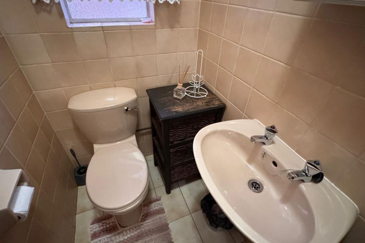 A compact guest bathroom featuring dated beige wall tiles, a matching toilet, and a pedestal basin.