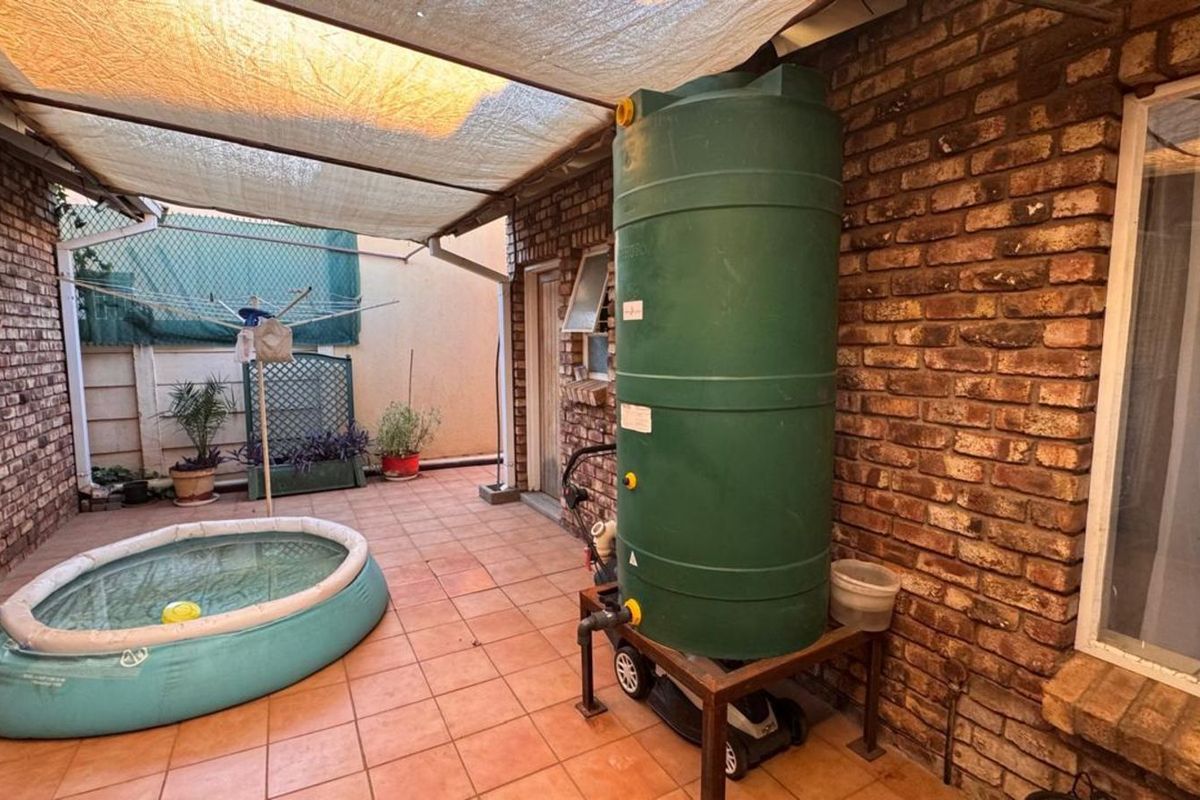 A paved rear courtyard area featuring a large water storage tank, covered patio space, and brick wall finishes.