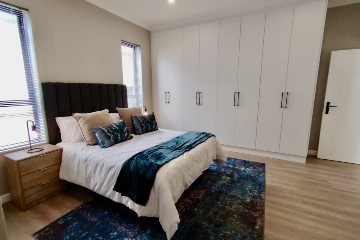 A well-maintained bedroom featuring modern built-in floor-to-ceiling wardrobes, neutral wall finishes, and light-toned wood-look flooring.