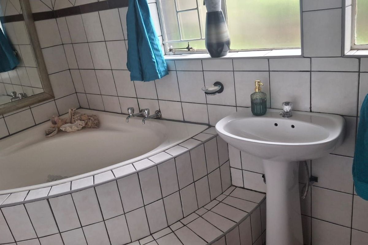 A functional bathroom featuring a tiled built-in corner bathtub and a white pedestal basin with wall-mounted fixtures.