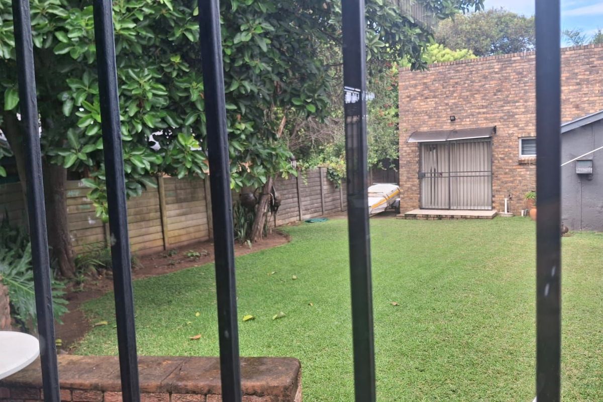 A private rear garden featuring a well-maintained lawn, mature trees, and a brick-faced exterior wall with a sliding door entrance.