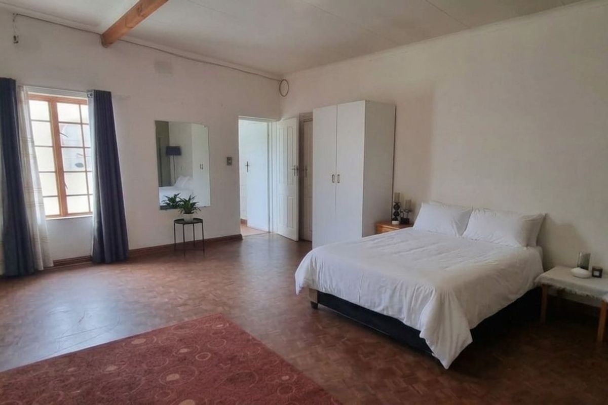 Spacious bedroom featuring parquet flooring, exposed ceiling beam, and large windows allowing for natural light.