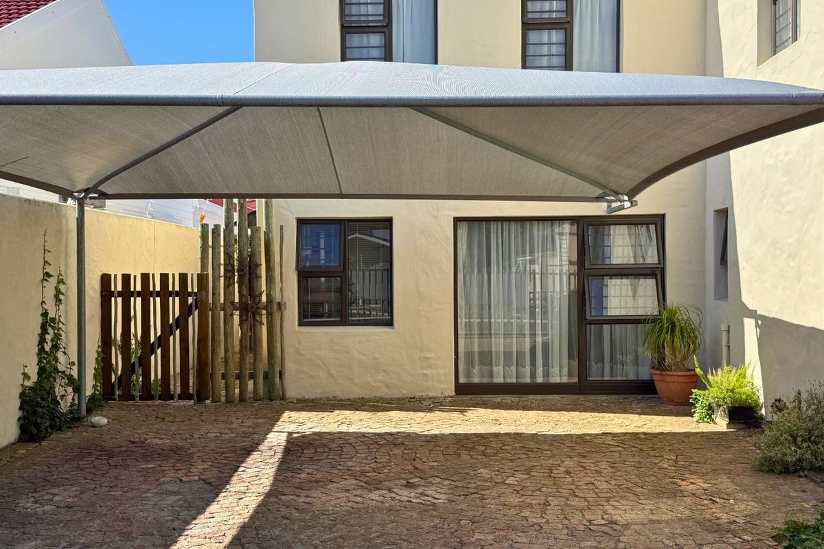 A paved outdoor area featuring a large shade sail, providing a covered space adjacent to the main building structure.