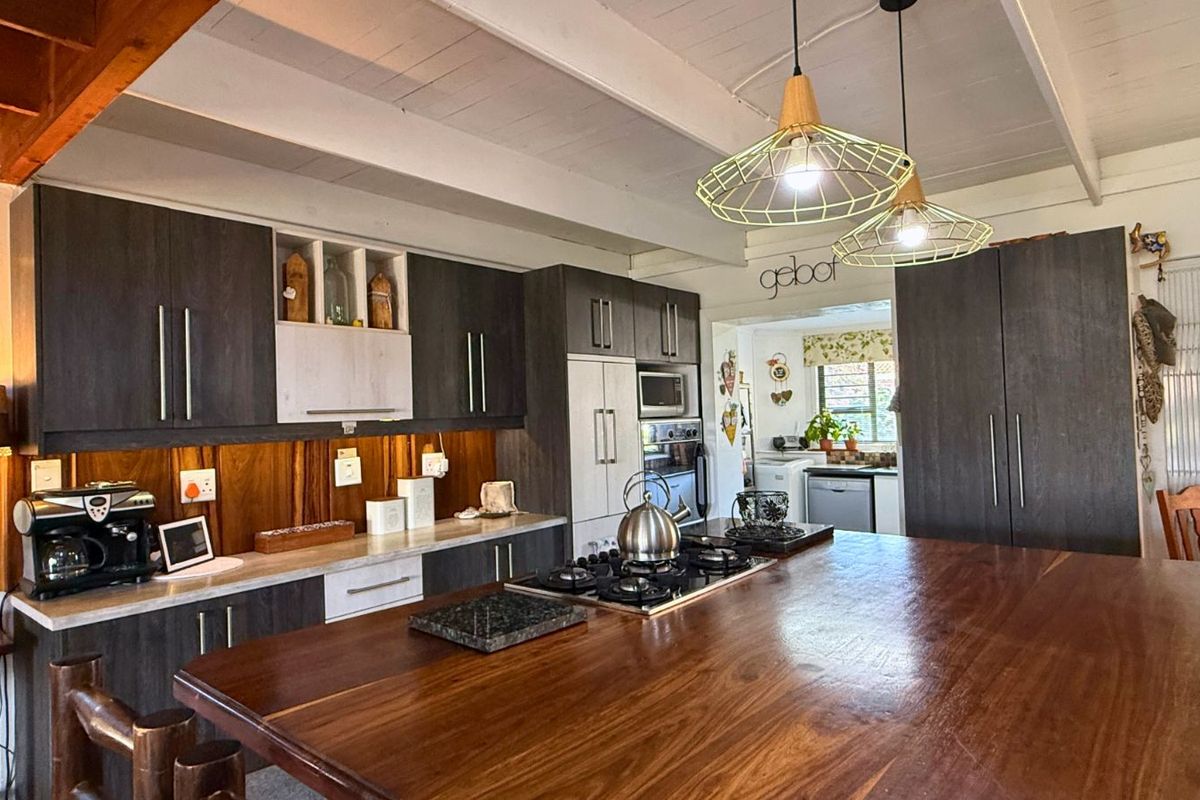 Modern kitchen featuring dark cabinetry, a large timber-topped island with an integrated gas hob, and exposed white timber ceiling beams.