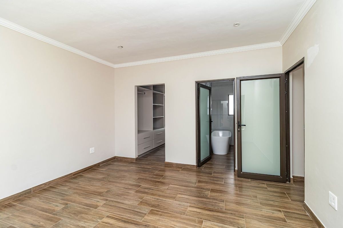A spacious bedroom featuring wood-look tile flooring, crown molding, an integrated walk-in closet, and an en-suite bathroom with a freestanding bathtub.