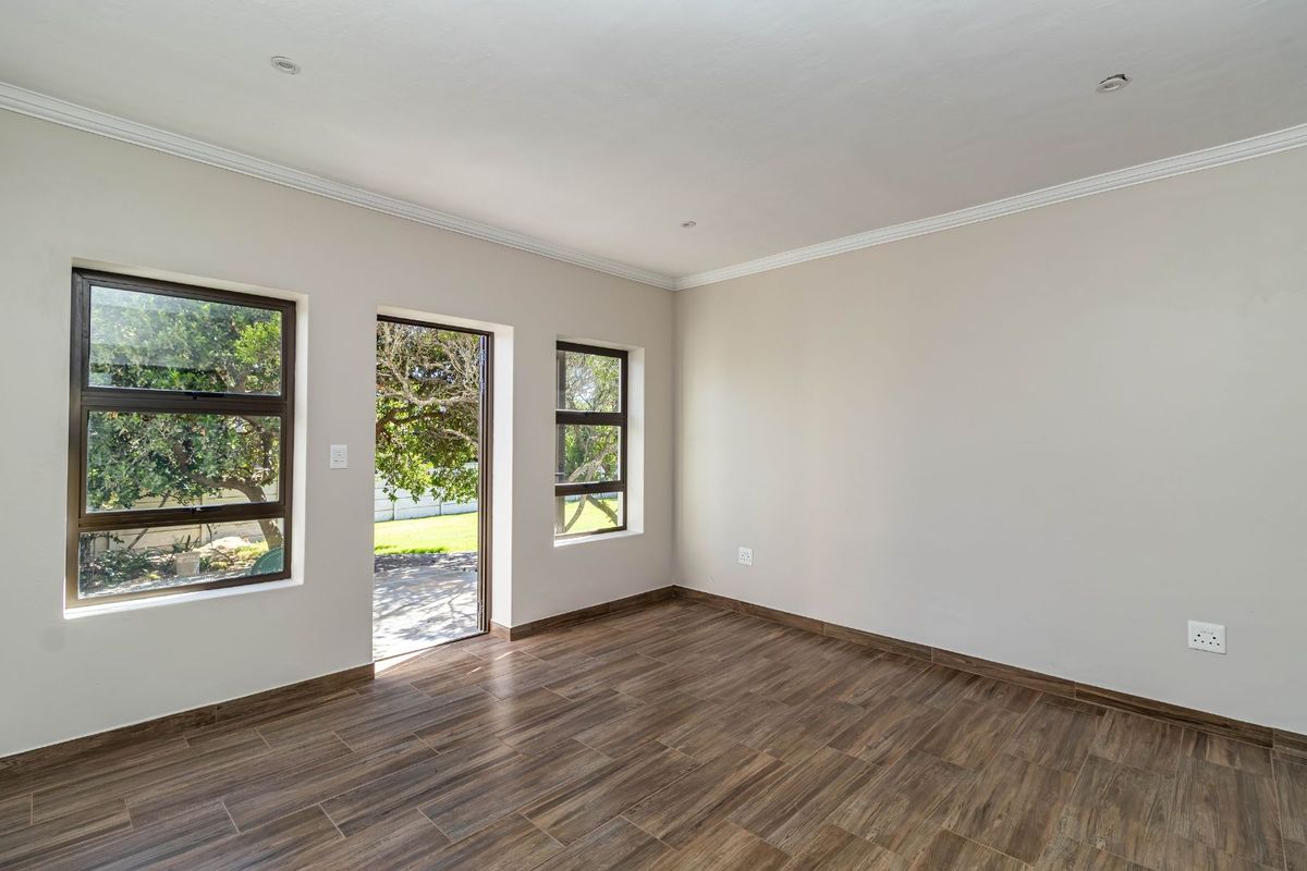 A bright, empty living room featuring modern wood-look tile flooring, recessed ceiling lighting, and direct access to an outdoor patio area.