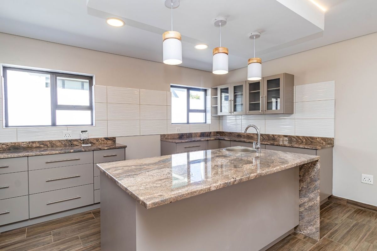 Modern kitchen featuring granite countertops, a central island with a prep sink, sleek cabinetry, and contemporary pendant lighting.