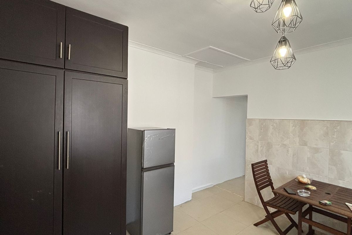 A functional kitchen area featuring dark cabinetry, tiled splashback, and neutral floor tiles, illuminated by modern geometric pendant lighting.