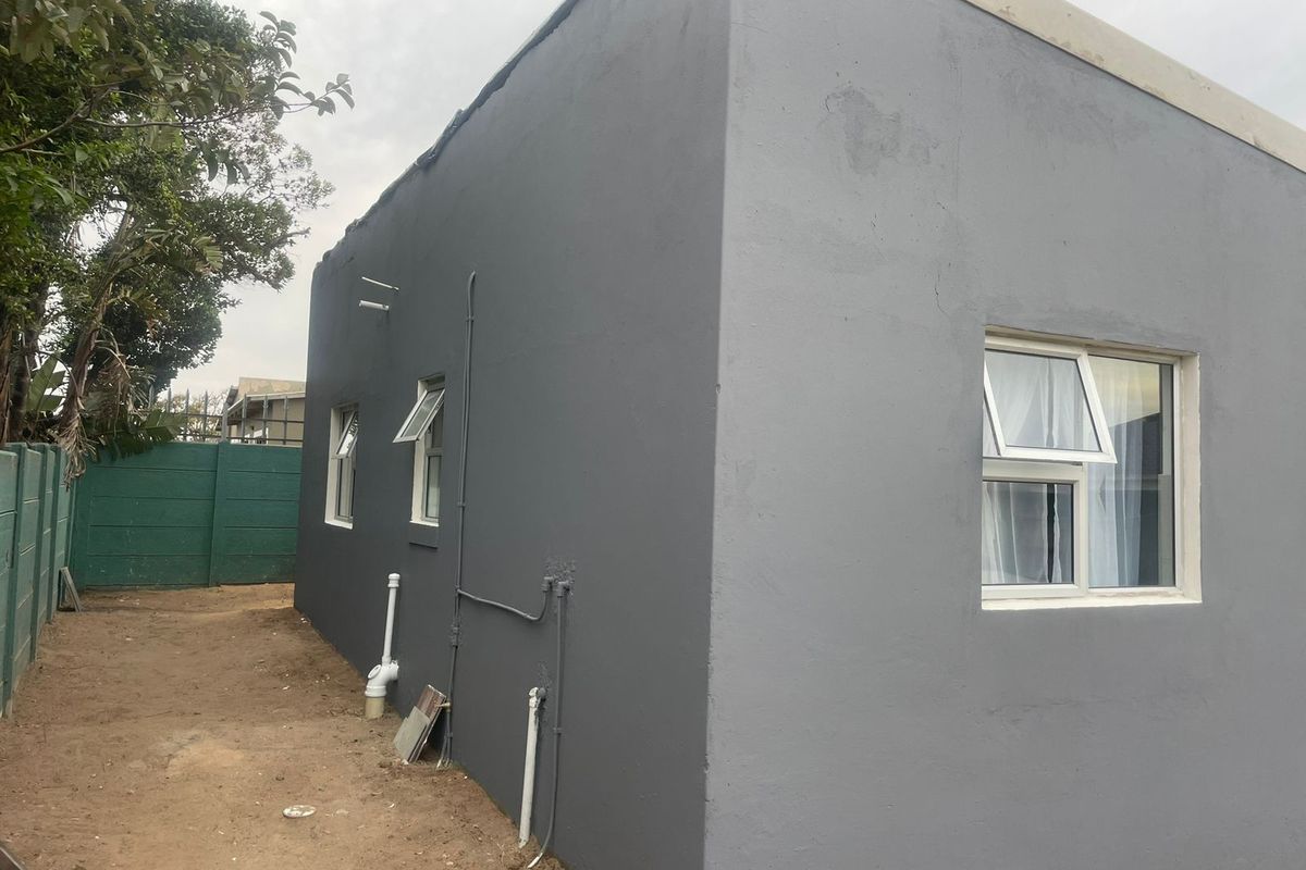 A view of the side exterior elevation of the house, featuring grey painted walls, white window frames, and exposed utility piping.
