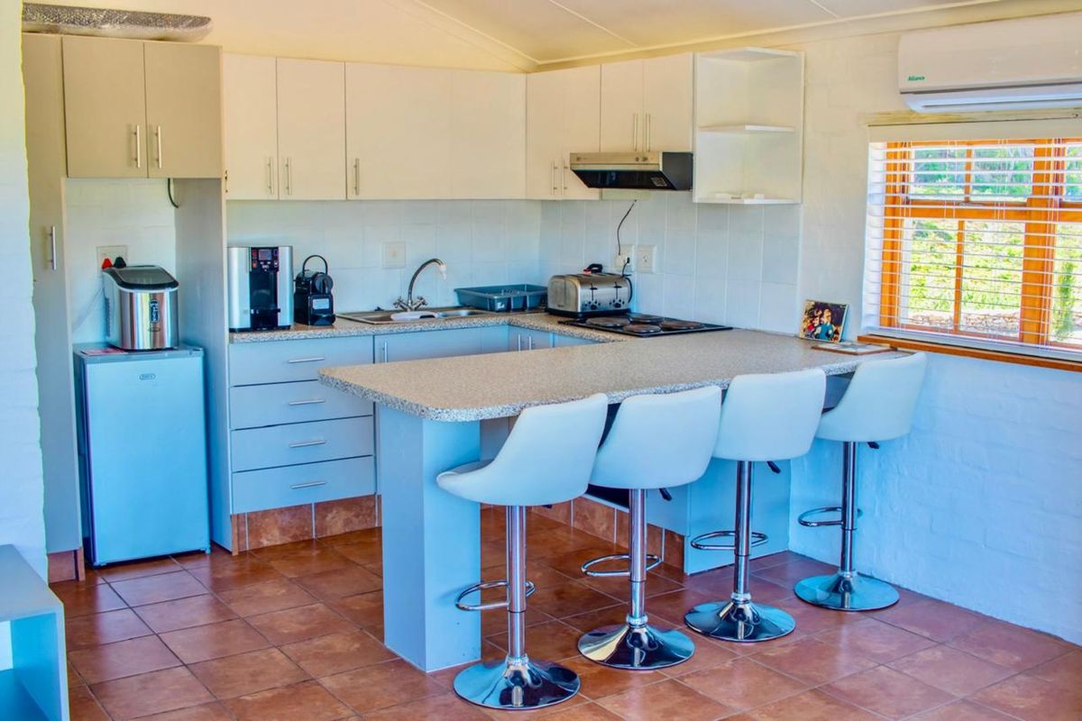 A compact kitchen featuring white cabinetry, a breakfast bar with seating, tiled flooring, and a built-in extractor fan.