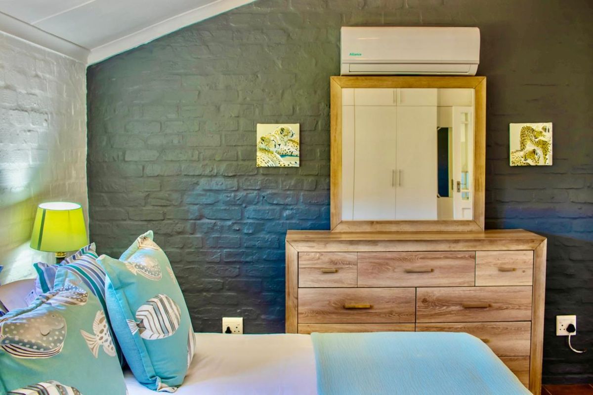A cozy bedroom featuring a dark painted brick feature wall, built-in cupboards, and a wall-mounted air conditioning unit.