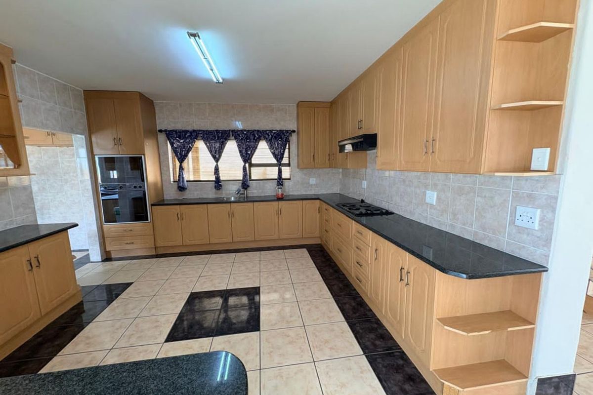 Spacious kitchen featuring light wood cabinetry, dark granite countertops, built-in oven, gas hob, and tiled flooring with decorative accents.
