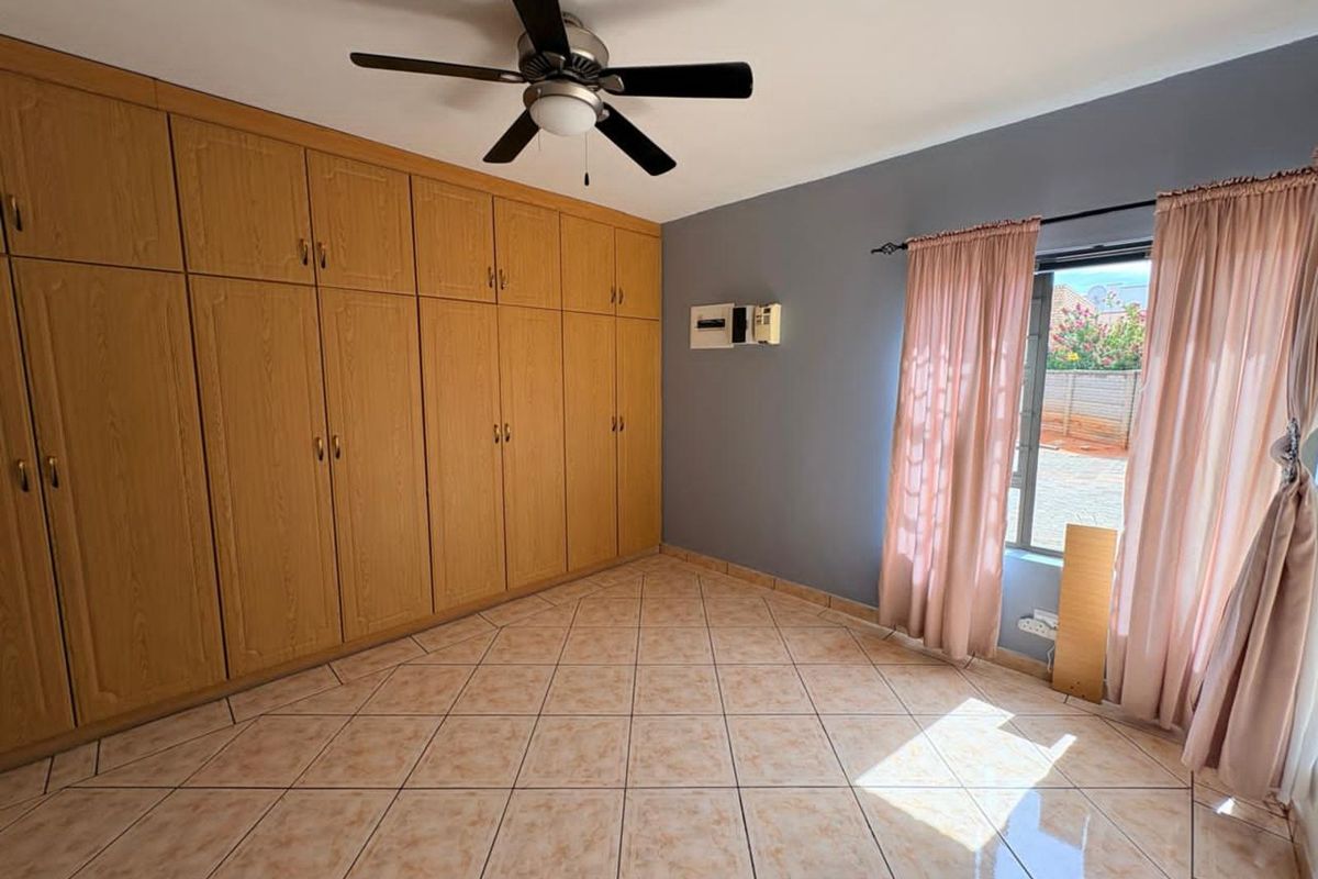 A bedroom featuring extensive built-in wooden cabinetry, tiled flooring, a ceiling fan, and a window with natural light.
