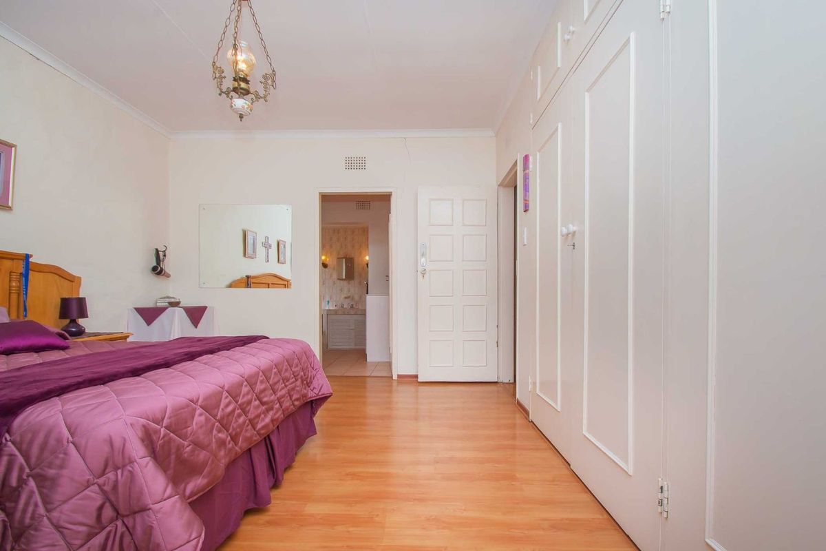 Spacious bedroom featuring built-in cupboards, laminate flooring, and direct access to an en-suite bathroom.