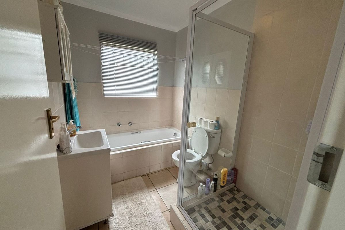 A functional bathroom featuring a built-in bathtub, a separate glass-enclosed shower, a vanity basin, and a toilet with neutral wall and floor tiling.