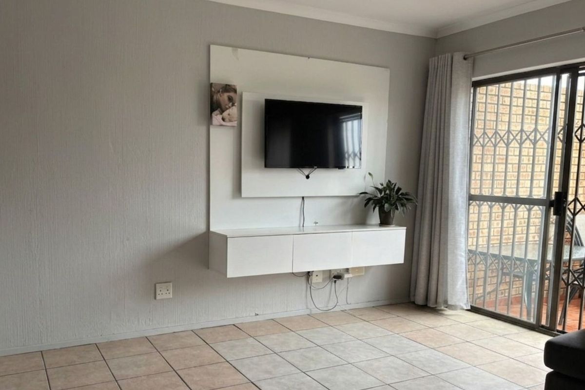 Living room featuring tiled flooring, a wall-mounted media unit, and sliding glass doors providing access to an outdoor patio area.