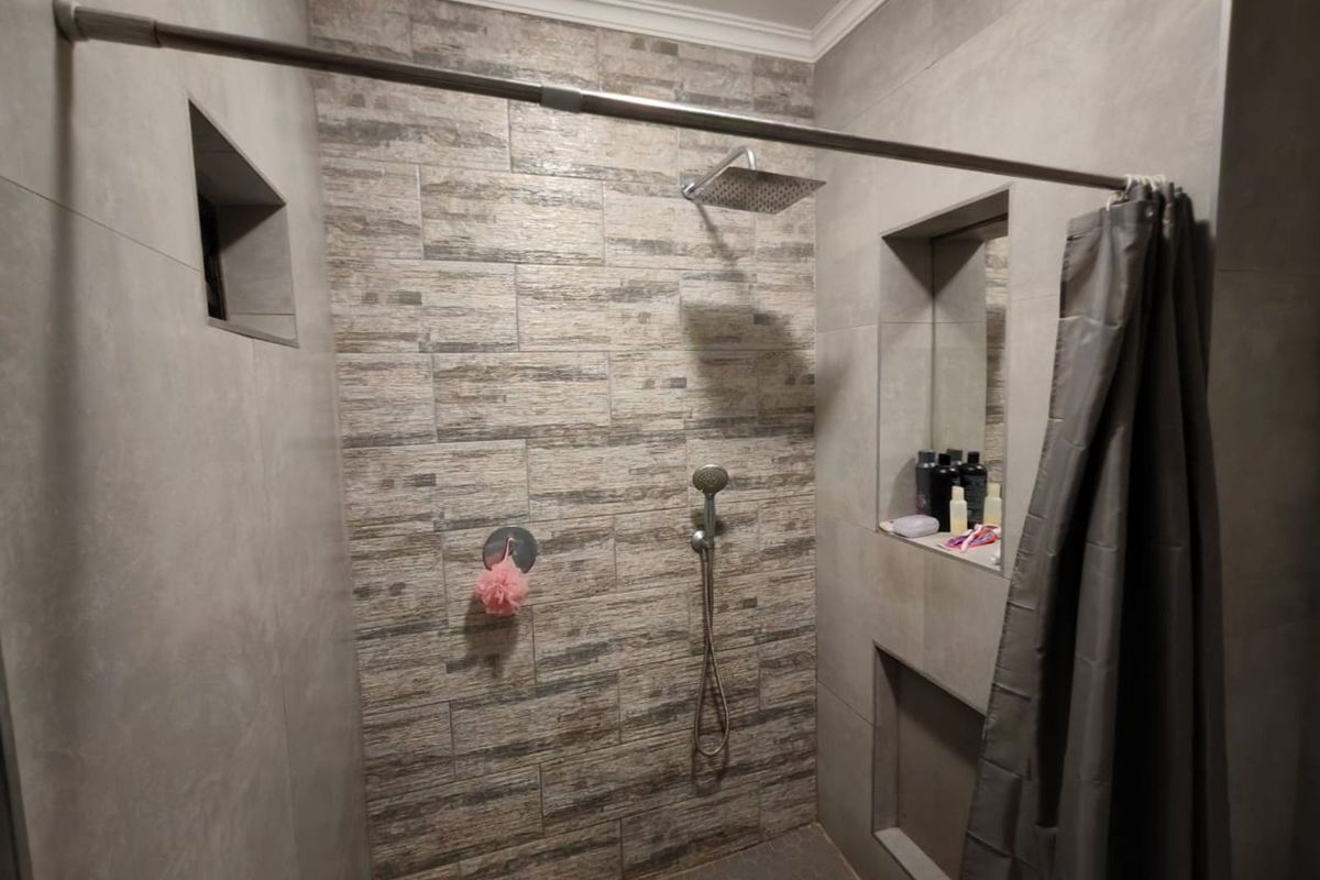 A modern shower enclosure featuring a rainfall showerhead, handheld shower attachment, and built-in wall niches for storage, finished with textured stone-look tiling.