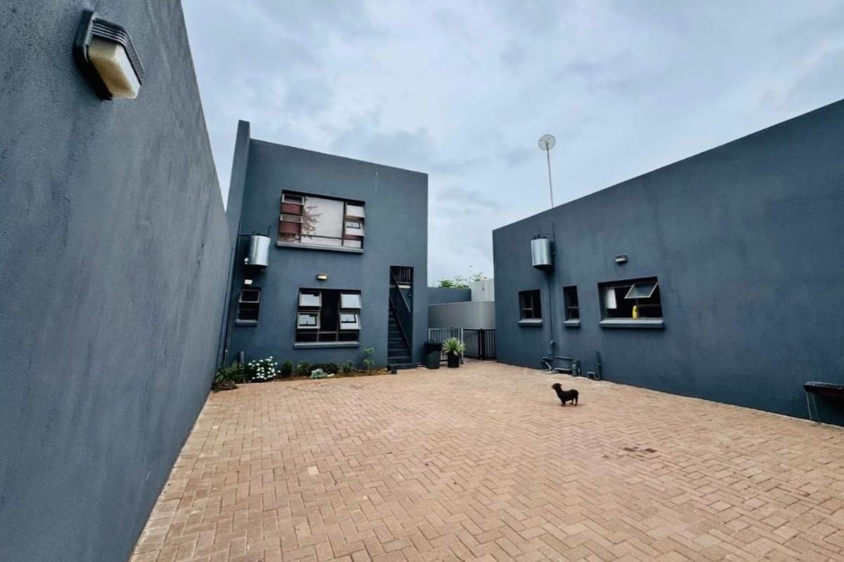A paved rear courtyard area featuring modern dark grey exterior walls, aluminium window frames, and external wall-mounted lighting fixtures.