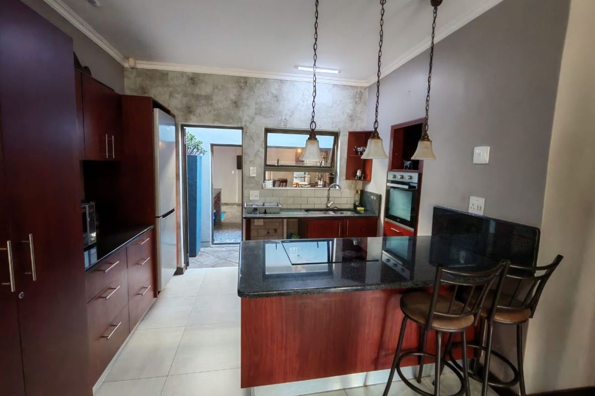 A functional kitchen featuring dark wood cabinetry, granite countertops, a central island with a built-in hob, and pendant lighting.