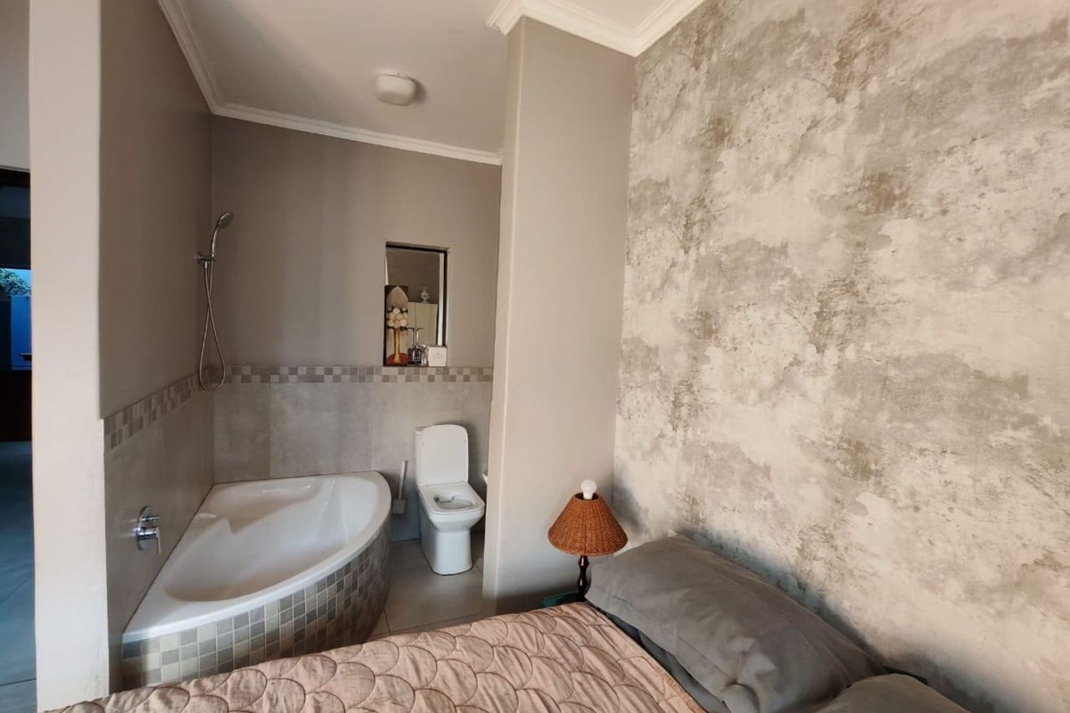 A bedroom featuring an open-plan en-suite bathroom with a corner bathtub, shower head, and toilet, finished with neutral tones and textured wall accents.