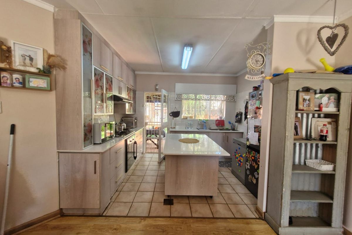 A functional kitchen featuring light wood-toned cabinetry, a central island with a stone countertop, and tiled flooring with direct access to the rear exterior.