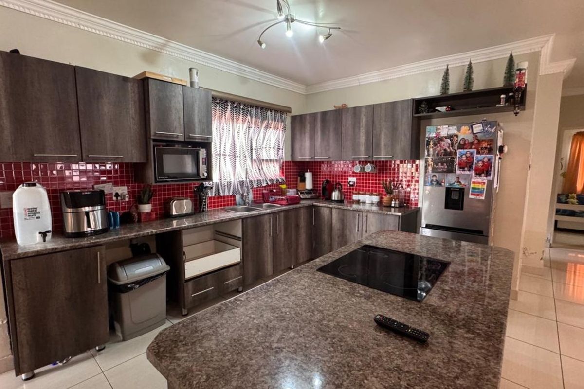 A functional kitchen featuring dark wood-grain cabinetry, a central island with a built-in induction cooktop, granite countertops, and a vibrant red tiled backsplash.