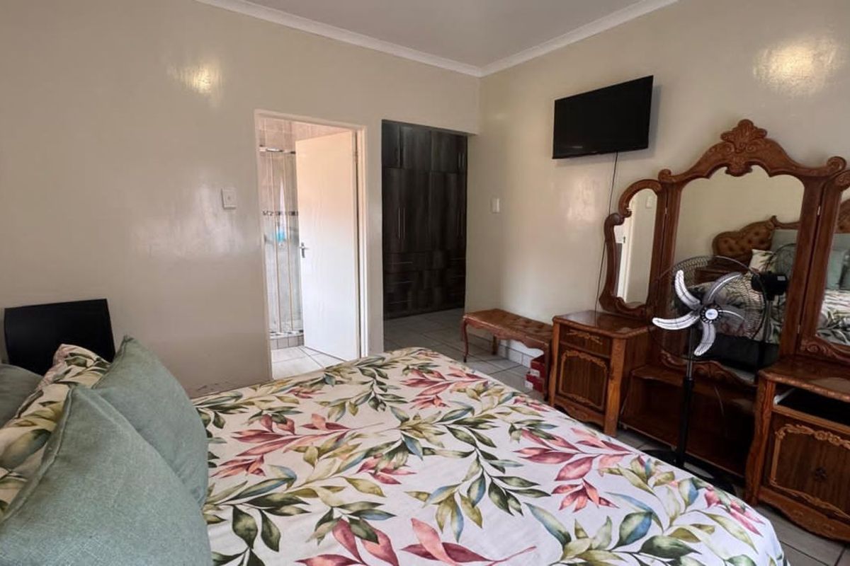 A bedroom featuring built-in cupboards and an en-suite bathroom access, finished with tiled flooring and neutral wall paint.