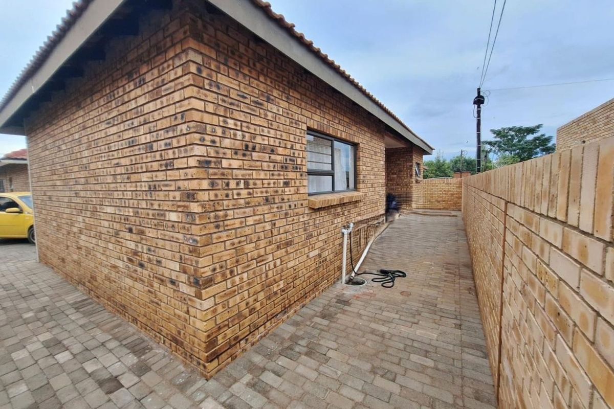 Side exterior view of the house featuring face brick walls, tiled roof, and paved walkway alongside a perimeter brick wall.