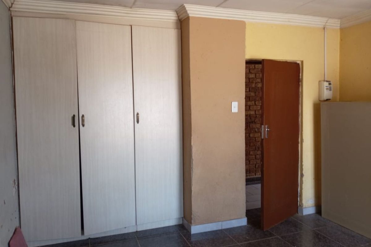 A bedroom featuring built-in white cabinetry, tiled flooring, and a doorway leading to an adjacent space with exposed brickwork.