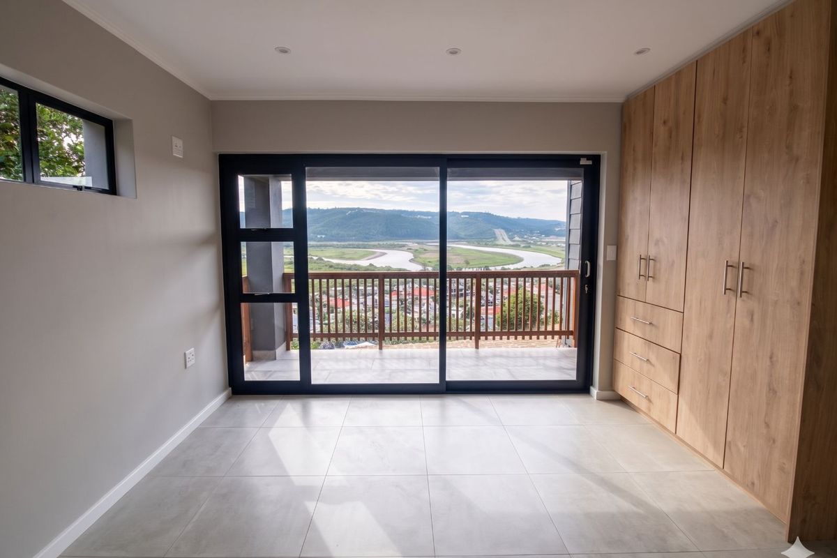 A bright, modern bedroom featuring built-in wooden cabinetry, tiled flooring, and large sliding glass doors opening to a balcony with scenic river and landscape views.