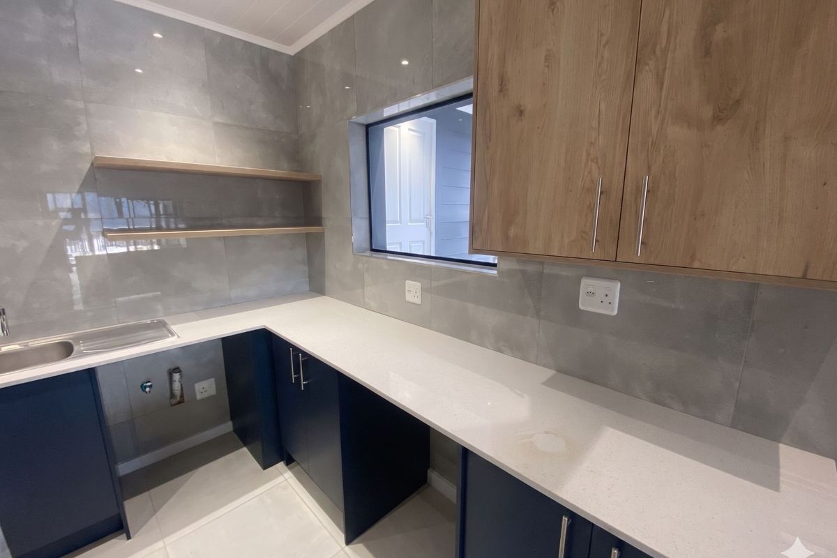 Modern kitchen featuring navy blue cabinetry, light wood-tone upper cabinets, stone-look countertops, grey tiled splashback, and integrated sink.