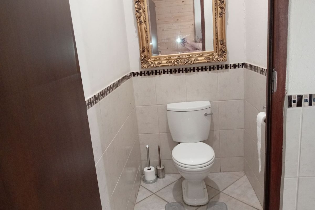 A compact guest bathroom featuring neutral wall tiles with a decorative border, tiled flooring, and a standard white toilet suite.