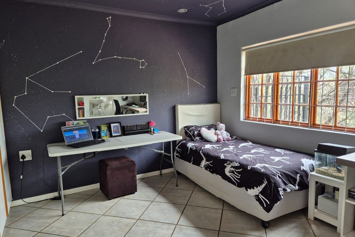 A bedroom featuring tiled flooring, a large window with security bars, and a dark-themed accent wall with constellation detailing.