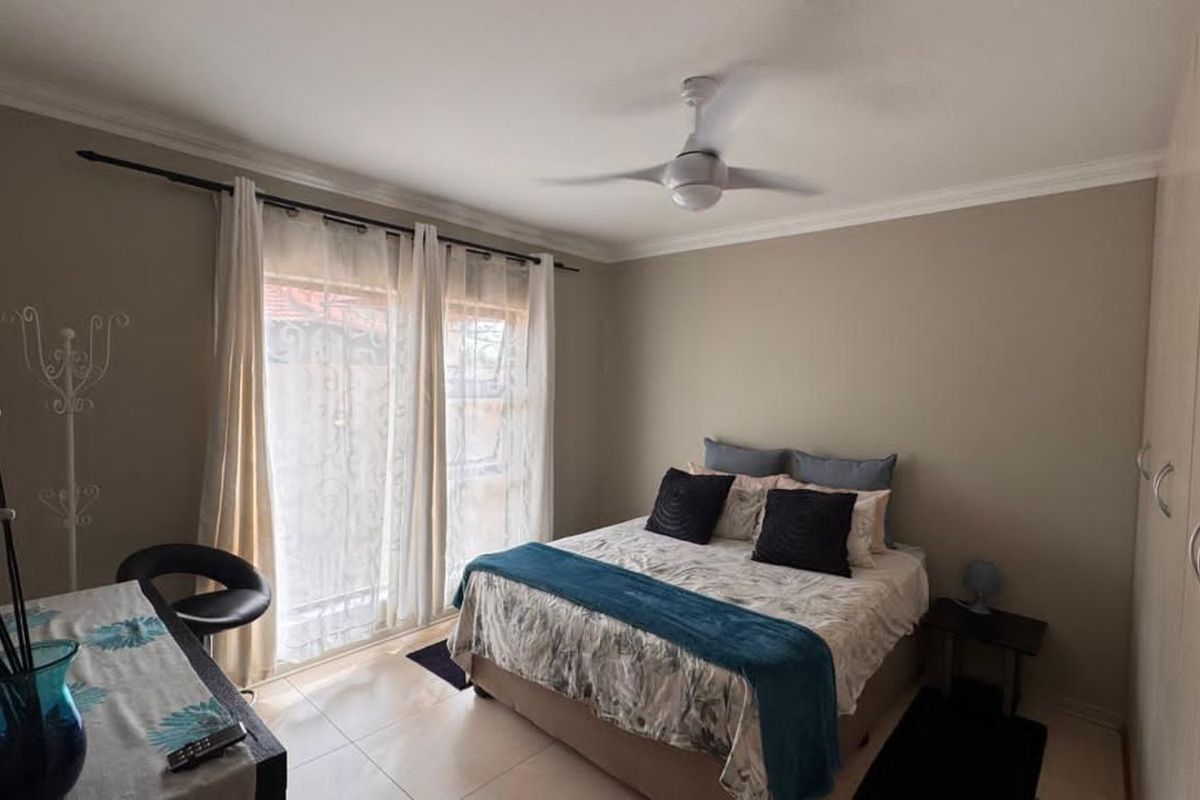 A well-maintained bedroom featuring tiled flooring, built-in cupboards, and a ceiling fan, with direct access to an outdoor area through sliding glass doors.