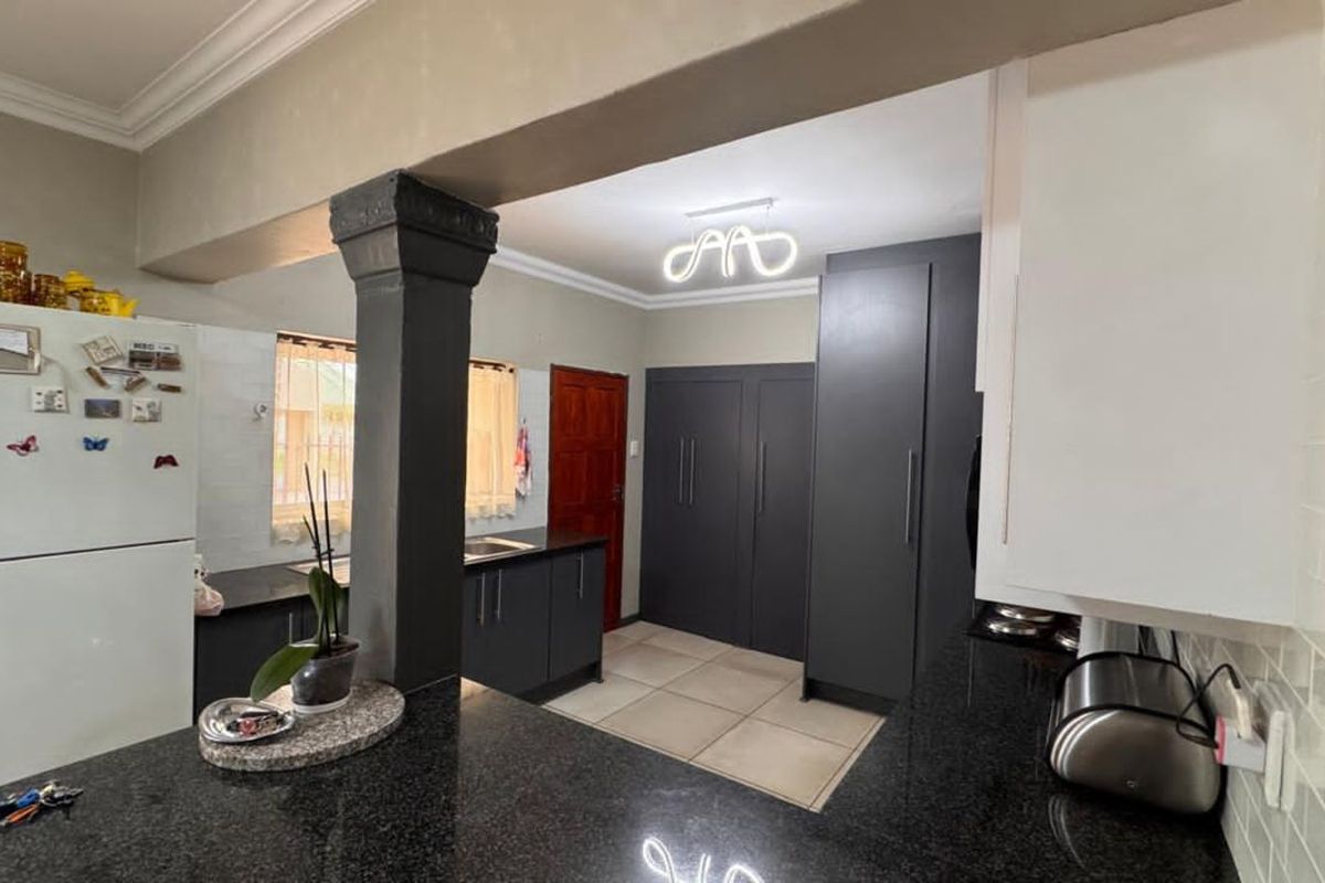 A modern kitchen featuring dark cabinetry, granite countertops, tiled flooring, and a central structural pillar, creating a functional and contemporary cooking space.
