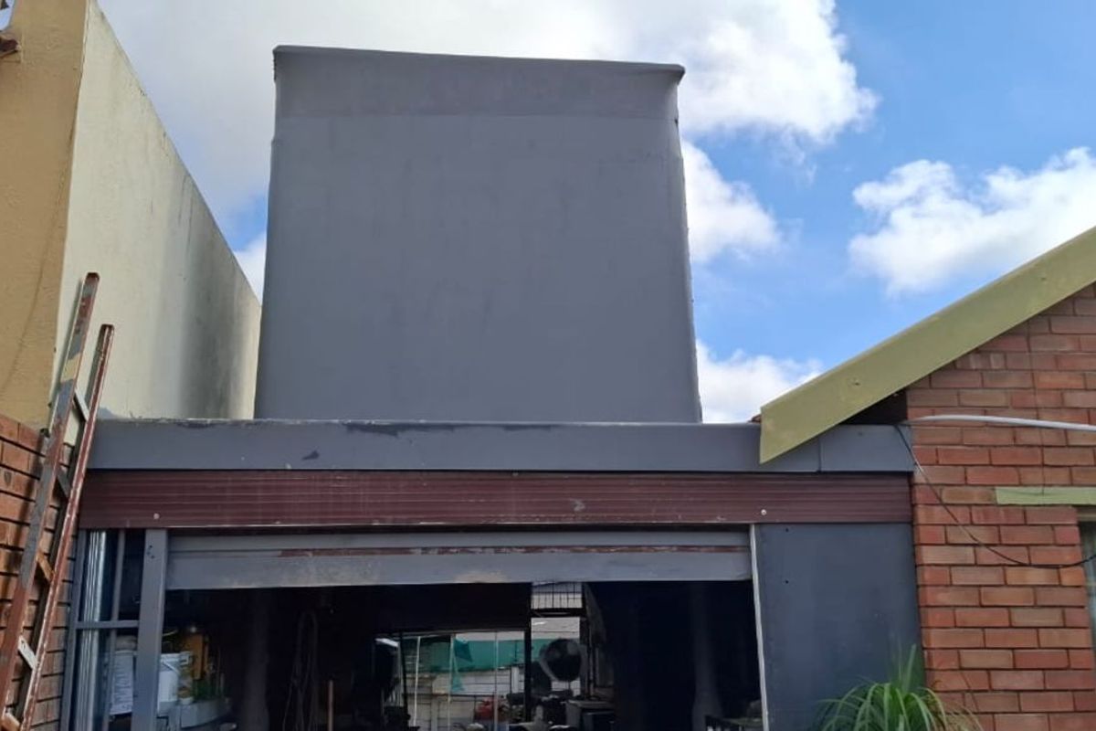 Rear view of the property showing a brick structure with a grey painted extension and visible signs of exterior wear.