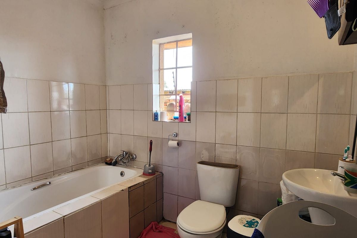 A dated bathroom featuring a built-in bathtub, standard toilet, and pedestal basin with tiled walls and a small window.
