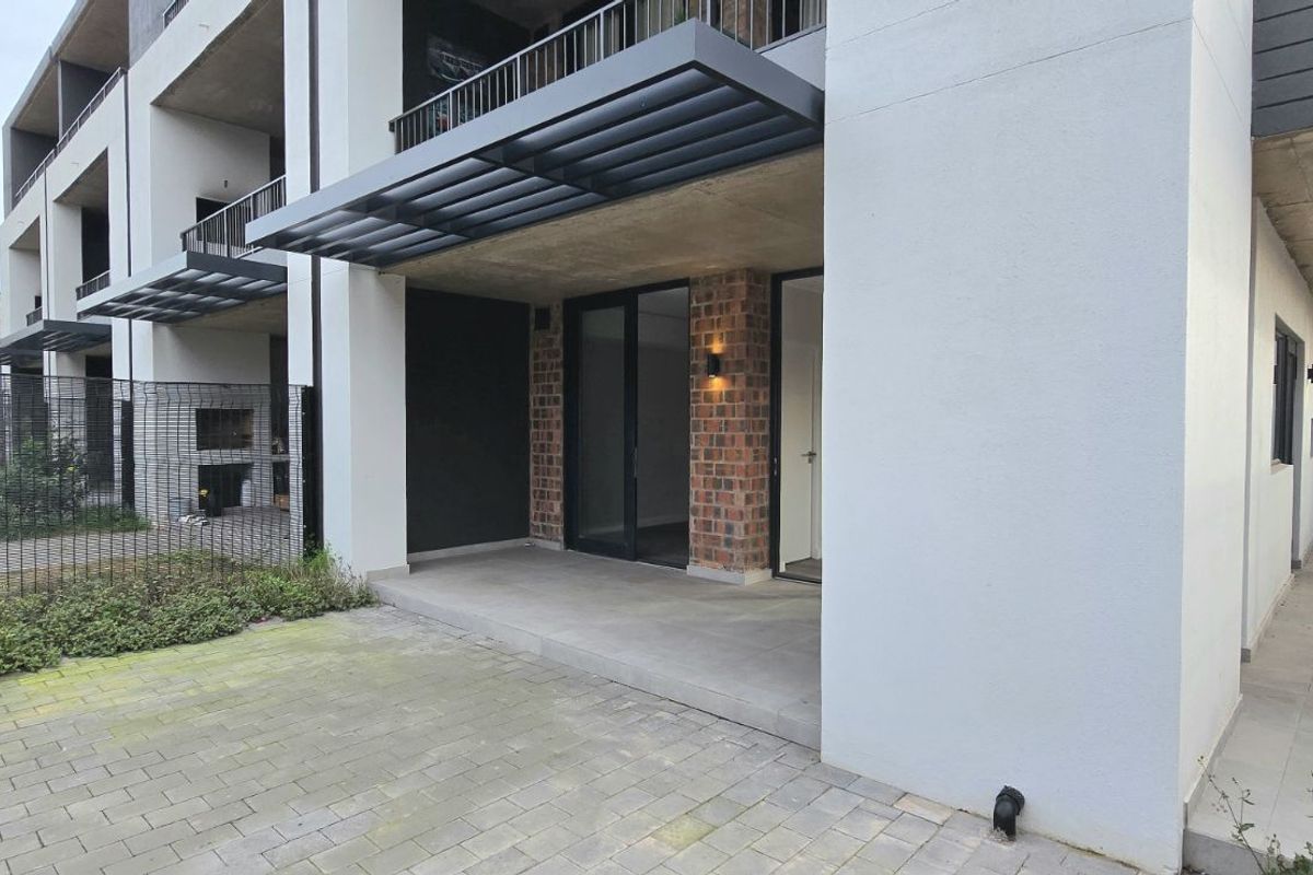 A modern ground-floor apartment exterior featuring a covered patio, brick accents, and a private paved courtyard area.