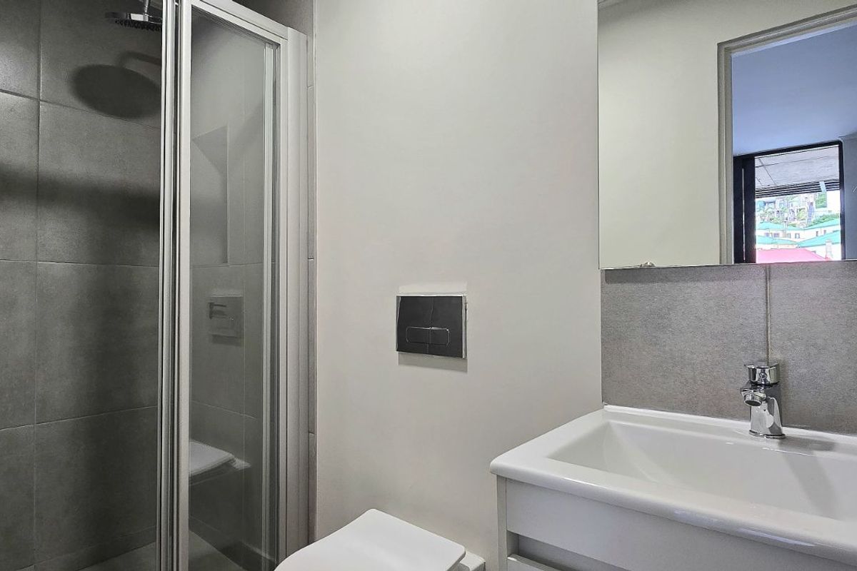 Modern bathroom featuring a glass-enclosed shower, wall-mounted toilet with concealed cistern, and a sleek vanity basin with a large mirror.