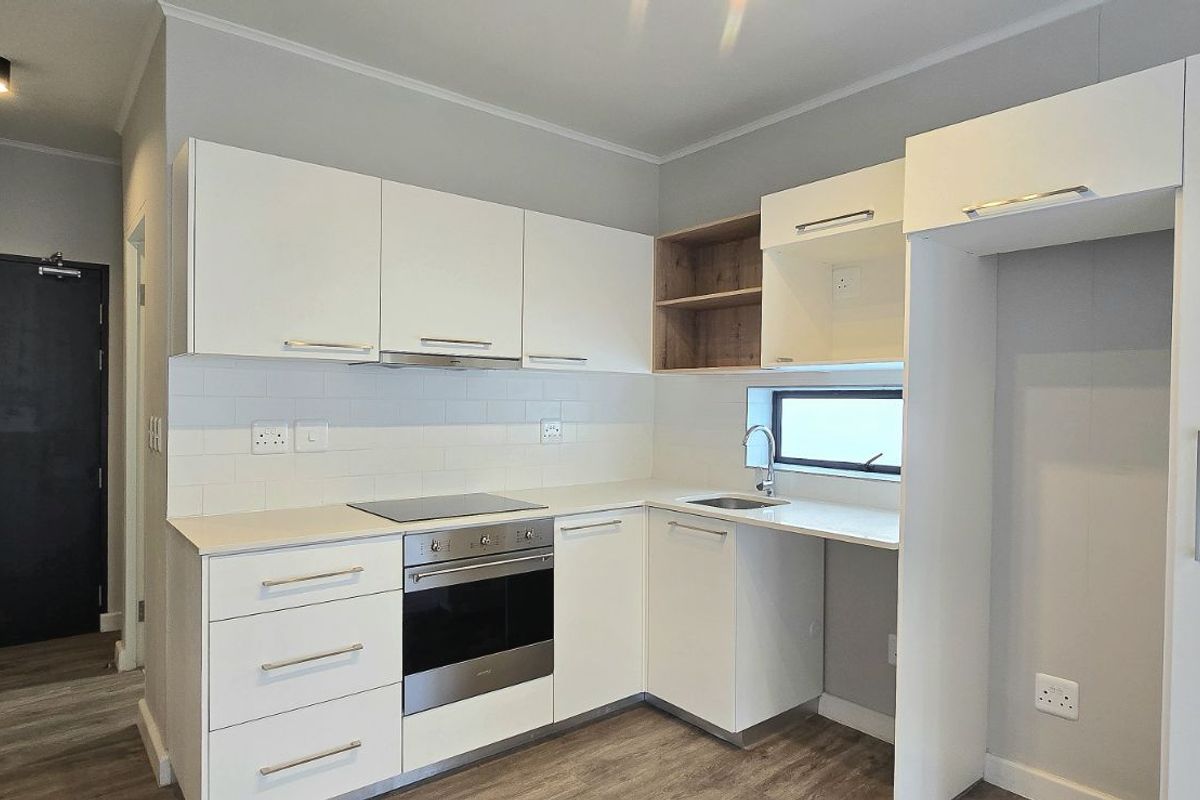 Modern kitchen featuring white cabinetry, built-in oven, electric hob, extractor fan, and a dedicated space for a refrigerator.