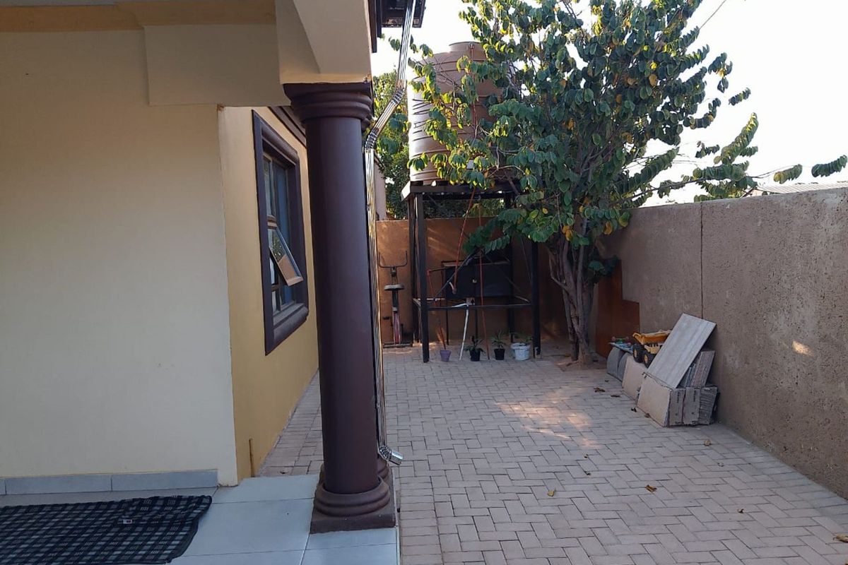 A paved side courtyard area featuring a structural column, a water storage tank on a metal stand, and perimeter boundary walls.