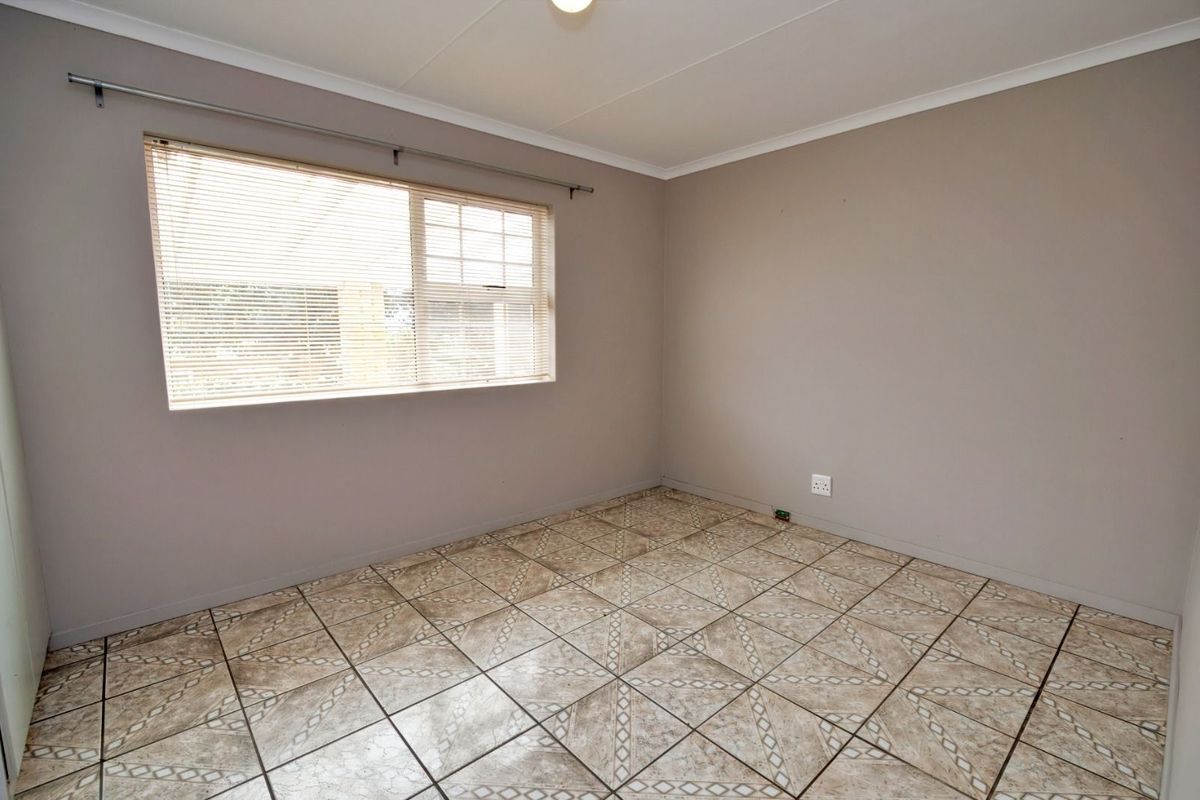 A clean, empty bedroom featuring neutral wall paint, tiled flooring, and a window fitted with horizontal blinds.
