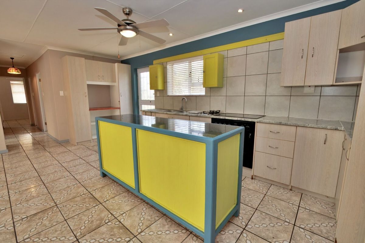 A functional kitchen featuring a central island, built-in cabinetry, tiled splashbacks, and a ceiling fan, offering a practical layout for daily meal preparation.