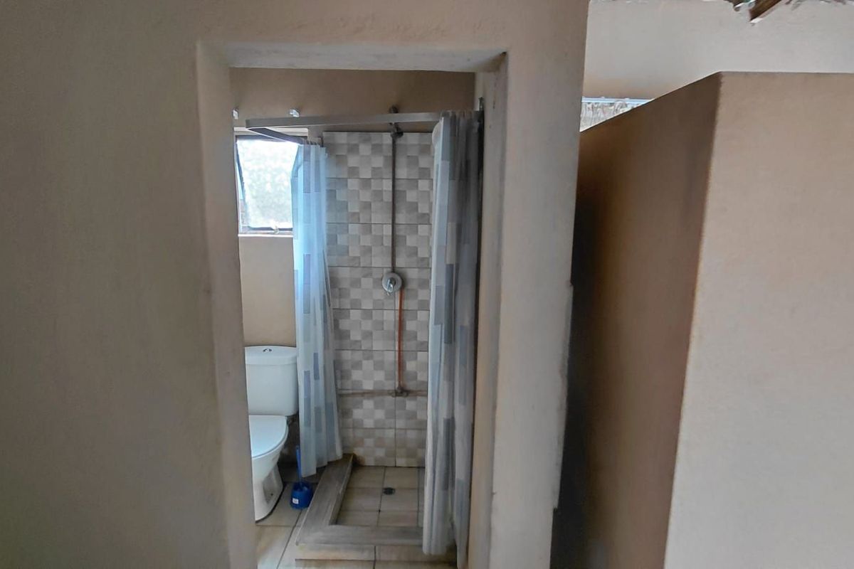 A compact bathroom featuring a tiled shower enclosure with exposed plumbing and a standard toilet, requiring cosmetic updates to improve the overall finish.