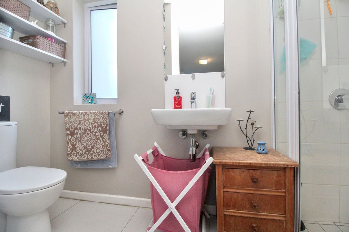 A functional bathroom featuring a wall-mounted basin, a shower enclosure with chrome fixtures, and tiled flooring.